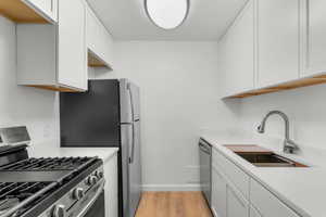 Kitchen featuring stainless steel appliances, light wood finished floors, white cabinets, and light stone counters