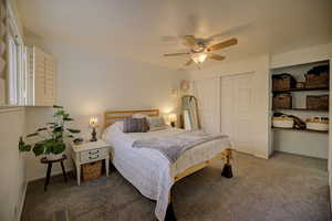 Carpeted primary bedroom featuring ceiling fan and a closet and shelves