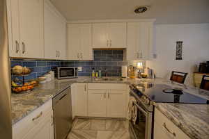 Kitchen featuring decorative backsplash, light stone counters, and light marble finish floors
