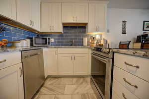 Kitchen with light stone countertops, stainless steel appliances, white cabinetry, and backsplash