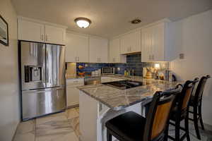 Kitchen featuring stainless steel appliances, a kitchen bar, a peninsula, with granite counters, and tasteful backsplash