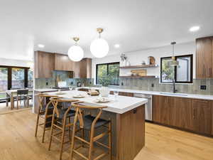 Kitchen with brown cabinetry, a breakfast bar, hanging light fixtures, plenty of natural light, and recessed lighting
