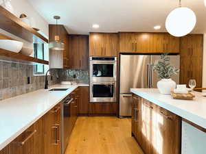Kitchen featuring pendant lighting, appliances with stainless steel finishes, light wood finished floors, brown cabinetry, and recessed lighting