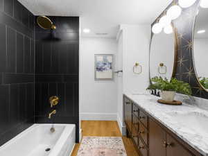 Full bathroom featuring double vanity, washtub / shower combination, and light wood finished floors