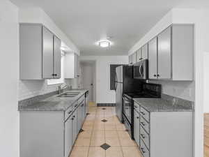 Kitchen featuring dark granite countertops, stainless steel appliances, light tile patterned floors, gray cabinetry, and backsplash