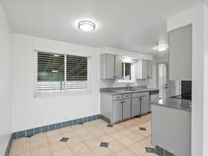 Kitchen with gray cabinets, light tile patterned floors, backsplash, and dishwasher