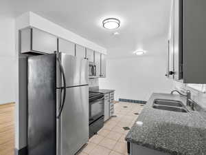 Kitchen featuring appliances with stainless steel finishes, gray cabinets, light tile patterned flooring, and dark granite counters