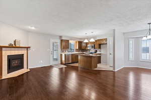 Kitchen featuring open floor plan, waterproof laminate, pendant lighting, a kitchen island, and a tiled fireplace