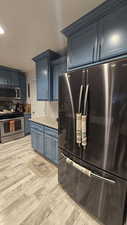Kitchen with appliances with stainless steel finishes, tasteful backsplash, blue cabinetry, light stone counters, and light wood finished floors