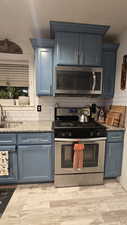 Kitchen featuring stainless steel appliances, light stone counters, blue cabinetry, and backsplash