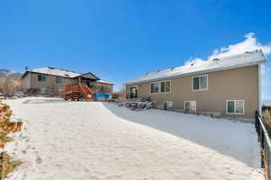 Snow covered back of property with a deck and stairs
