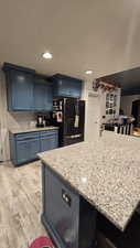 Kitchen with blue cabinetry, light stone counters, freestanding refrigerator, decorative backsplash, and recessed lighting