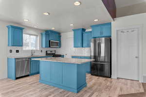 Kitchen with blue cabinetry, stainless steel appliances, light stone counters, recessed lighting, and a textured ceiling