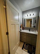 Half bathroom with a textured ceiling, vanity, and light tile patterned floors