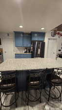 Kitchen with blue cabinetry, a breakfast bar area, decorative backsplash, a center island, and freestanding refrigerator