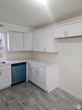 Kitchen featuring white cabinets, wood finish floors, dishwashing machine, light countertops, and a textured ceiling