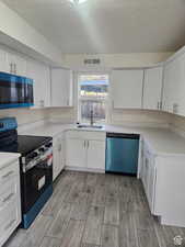 Kitchen featuring stainless steel electric stove, white cabinets, wood tiled floors, dishwashing machine, and a textured ceiling