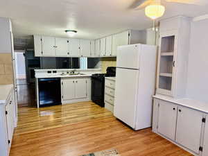 Kitchen featuring black appliances, white cabinets, light countertops, and light wood-style flooring