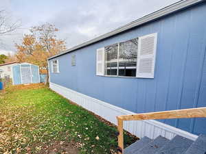 View of side of home featuring a lawn and a storage shed