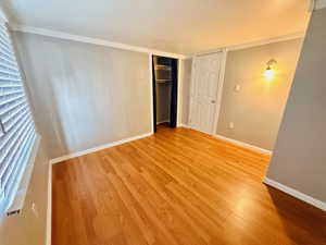 Unfurnished bedroom featuring light wood-type flooring, a closet, and crown molding