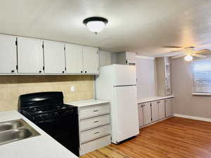 Kitchen with black gas stove, freestanding refrigerator, light countertops, a ceiling fan, and light wood-style floors