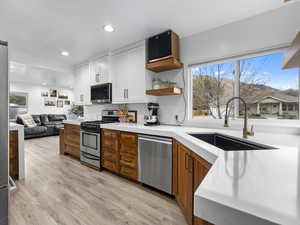 Kitchen with open floor plan, open shelves, appliances with stainless steel finishes, light wood finished floors, and recessed lighting