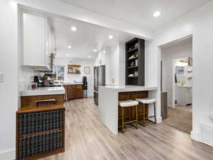 Kitchen with open shelves, white cabinetry, brown cabinets, a breakfast bar area, and recessed lighting