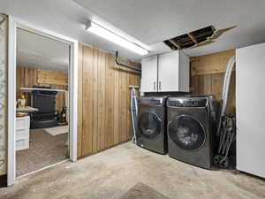 Washroom featuring wood walls, a textured ceiling, unfinished concrete flooring, washer and dryer, and cabinet space