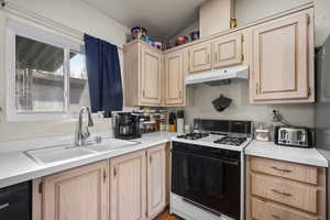 Kitchen featuring light brown cabinetry, gas range oven, light countertops, under cabinet range hood, and freestanding refrigerator