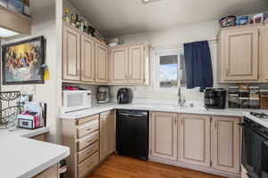 Kitchen with light brown cabinetry, light countertops, range with gas stovetop, and dishwasher