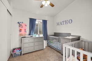 Bedroom featuring light colored carpet, a crib, ceiling fan, vaulted ceiling, and a closet
