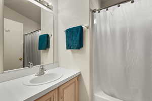 Bathroom featuring vanity, shower / bath combination with curtain, and a textured wall