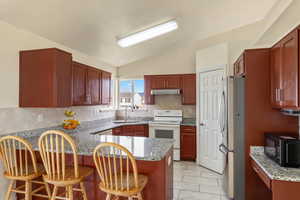 Kitchen with white electric range oven, freestanding refrigerator, dark stone countertops, black microwave, and lofted ceiling