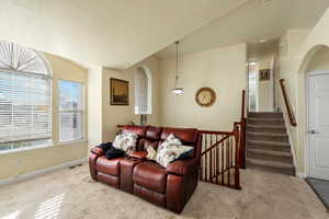 Carpeted living room featuring vaulted ceiling, stairway, and a textured ceiling