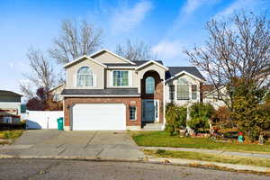 View of front facade featuring a gate, driveway, a garage, brick siding, and roof with shingles