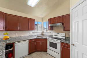 Kitchen featuring white appliances, vaulted ceiling, light tile patterned floors, under cabinet range hood, and dark stone counters
