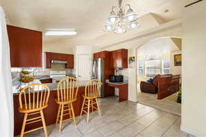 Kitchen featuring a kitchen breakfast bar, lofted ceiling, arched walkways, a peninsula, and decorative light fixtures