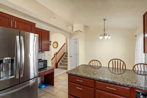 Kitchen featuring stainless steel fridge, reddish brown cabinets, dark stone counters, lofted ceiling, and a textured ceiling