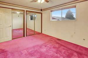 Unfurnished bedroom with multiple closets, a textured ceiling, carpet floors, ceiling fan, and crown molding