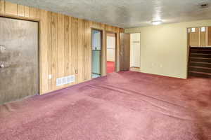 Unfurnished living room with wooden walls, carpet, and a textured ceiling