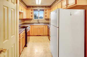 Kitchen featuring freestanding refrigerator, dark countertops, stainless steel electric range, open shelves, and backsplash