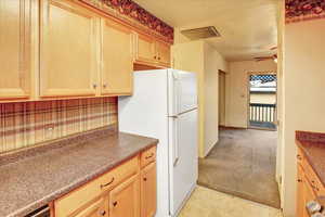 Kitchen with light carpet, freestanding refrigerator, backsplash, light brown cabinets, and a ceiling fan