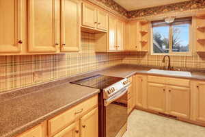 Kitchen with stainless steel range with electric cooktop, light brown cabinetry, open shelves, and decorative backsplash