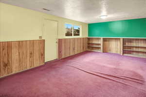 Carpeted spare room with wood walls, wainscoting, and a textured ceiling
