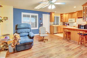 Kitchen featuring light countertops, a breakfast bar, open shelves, light wood-type flooring, and white appliances