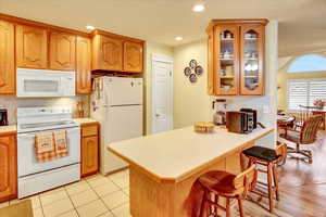 Kitchen featuring light countertops, white appliances, a breakfast bar area, a peninsula, and glass insert cabinets