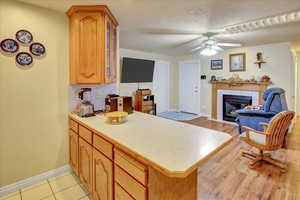 Kitchen featuring light countertops, a tiled fireplace, a peninsula, glass insert cabinets, and ceiling fan