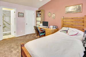 Bedroom with an office area, light colored carpet, ceiling fan, and ensuite bath