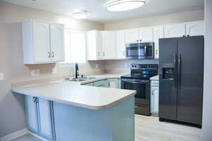 Kitchen featuring stainless steel appliances, a peninsula, white cabinets, and light countertops