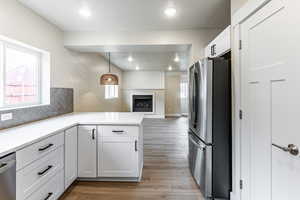 Kitchen with white cabinetry, stainless steel appliances, light wood-style floors, pendant lighting, and open floor plan